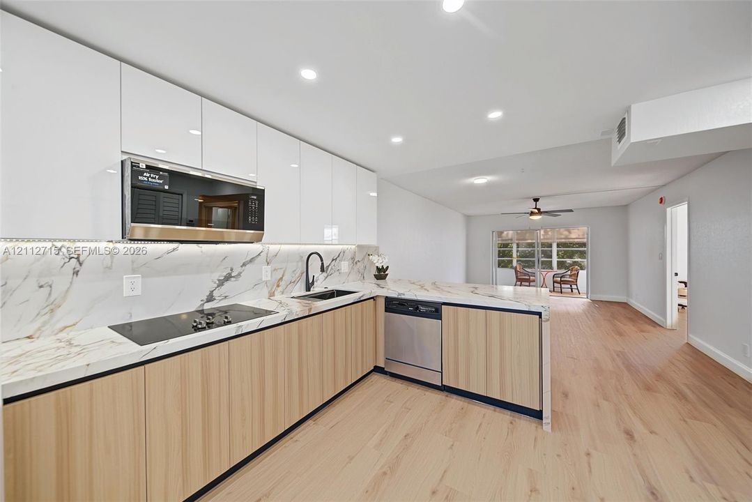 Kitchen featuring flat-panel cabinetry with a two-tone finish, stone-patterned backsplash and countertops, recessed lighting, and stainless steel appliances