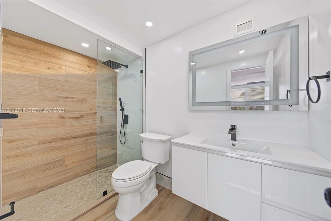 Walk-in shower featuring a glass enclosure, wood-finish tile wall, and rainfall showerhead, paired with a white floating vanity, quartz countertop, and integrated LED-lit mirror