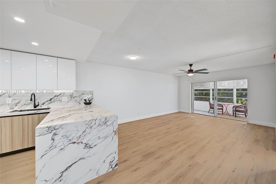 Kitchen featuring gloss white upper cabinetry, stone-patterned waterfall countertop, matte black faucet, and wood-finish flooring with an integrated ceiling fan and sliding glass doors