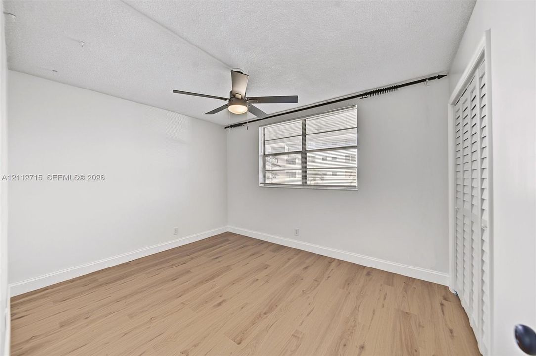 Interior room featuring wood-finish flooring, a ceiling fan with integrated lighting, a metal-framed window, and white louvered bifold closet doors