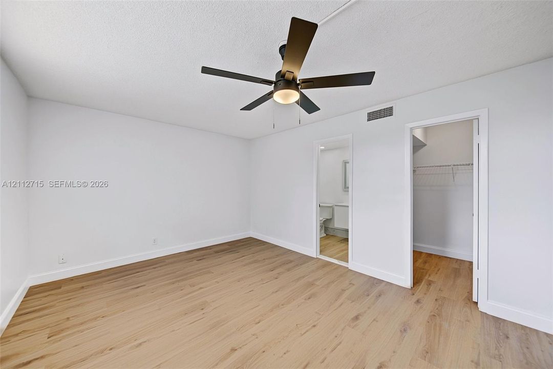 Room featuring wood-finish flooring, a dark-finish ceiling fan with integrated light fixture, and walk-in closet storage with built-in shelving