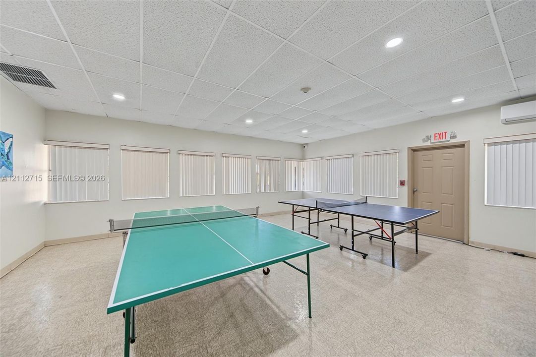 Spacious interior featuring a suspended drop ceiling, recessed lighting, neutral wall-to-wall flooring, multiple windows with vertical blinds, and a wall-mounted ductless HVAC unit