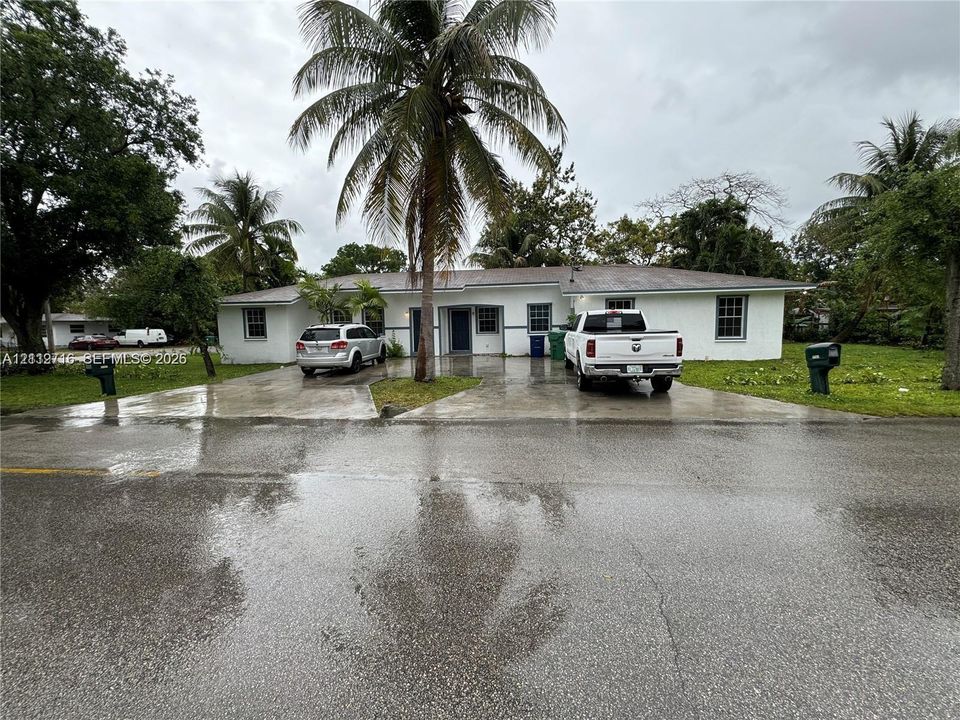Single-story residence featuring a white exterior, hip roof, dual paved driveways, and mature palm trees