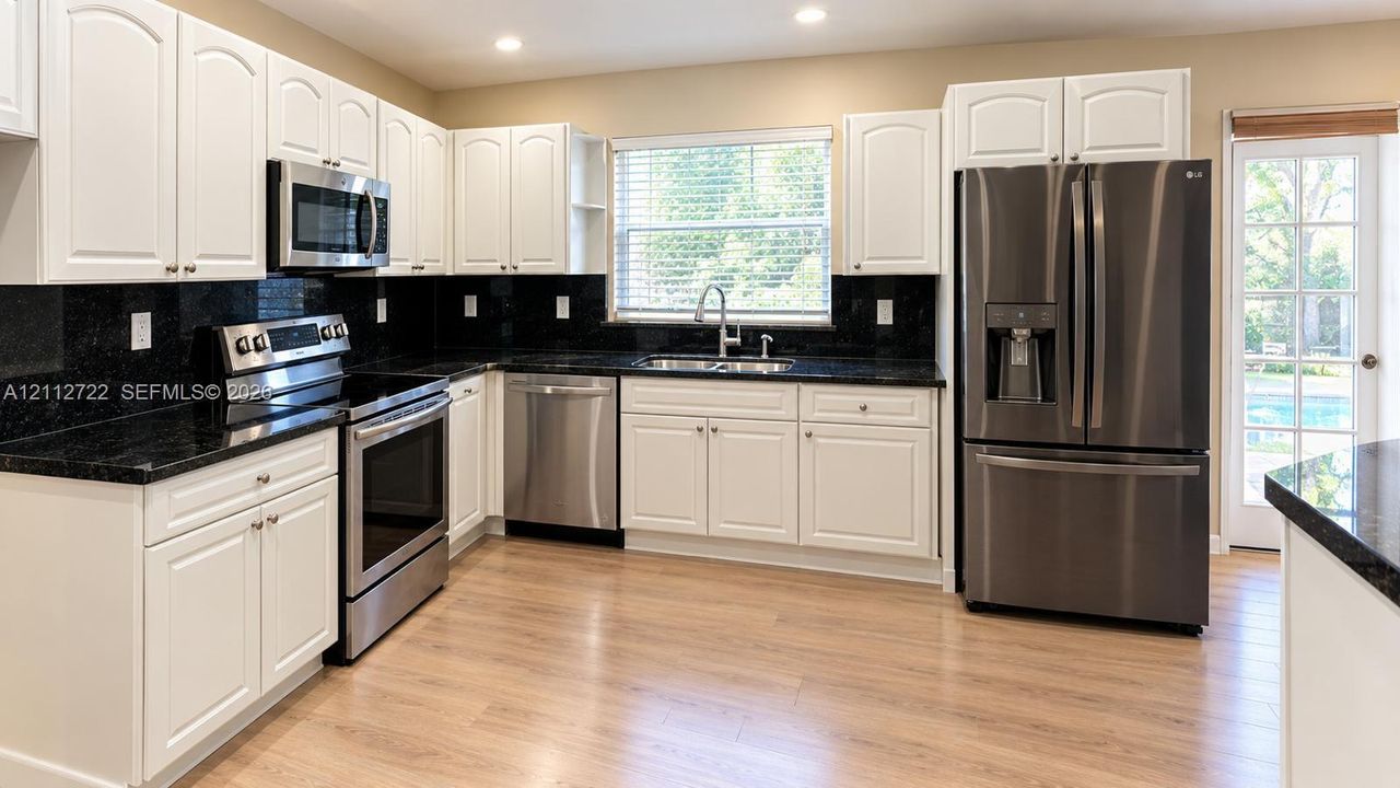 Kitchen featuring white shaker-style cabinetry, dark stone countertops, stainless steel appliances, and wood-finish flooring