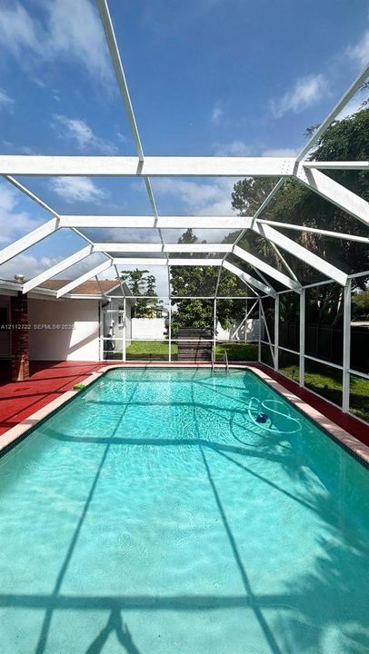 In-ground swimming pool enclosed by a white-frame screen structure featuring a red painted deck and fenced perimeter