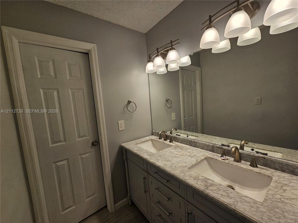 Bathroom vanity featuring dual under-mount sinks, stone-patterned countertops, gray cabinetry with metallic hardware, and two multi-bulb overhead light fixtures