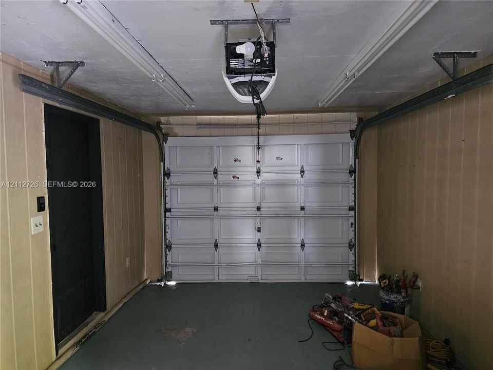 Enclosed garage featuring panelled wall cladding, a motorized overhead door, and dual linear light fixtures