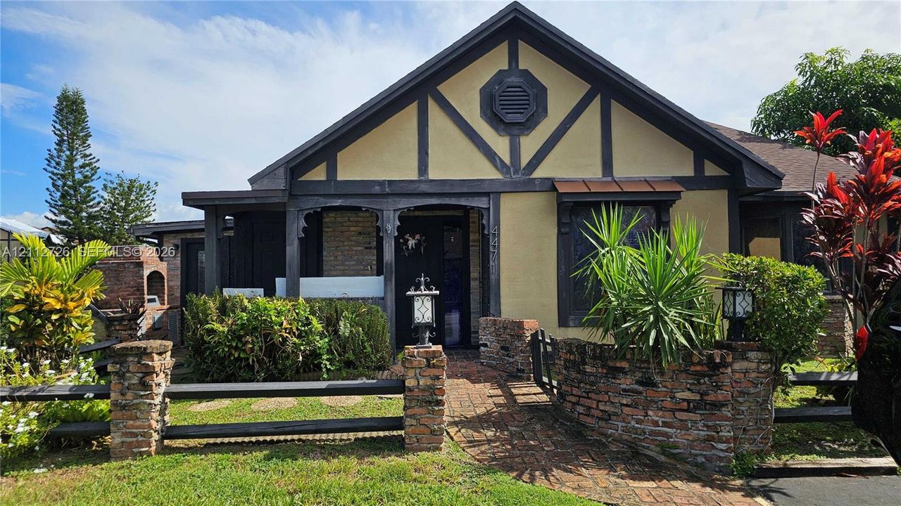 Tudor-inspired exterior featuring decorative timber framing, a brick-paved walkway, a stone-accented perimeter wall, and a built-in outdoor masonry grill