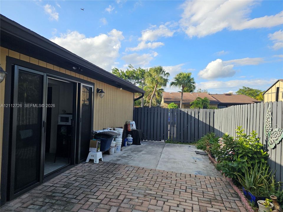 Rear exterior space featuring a herringbone-patterned brick patio, concrete slab extension, and vertical wood-style siding