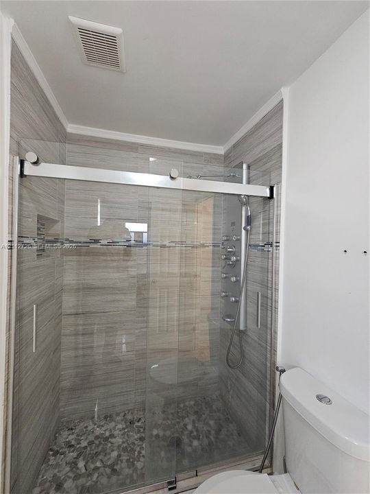 Walk-in shower featuring horizontal tile walls, a multi-head body spray system, a glass sliding door, and a pebble-stone floor