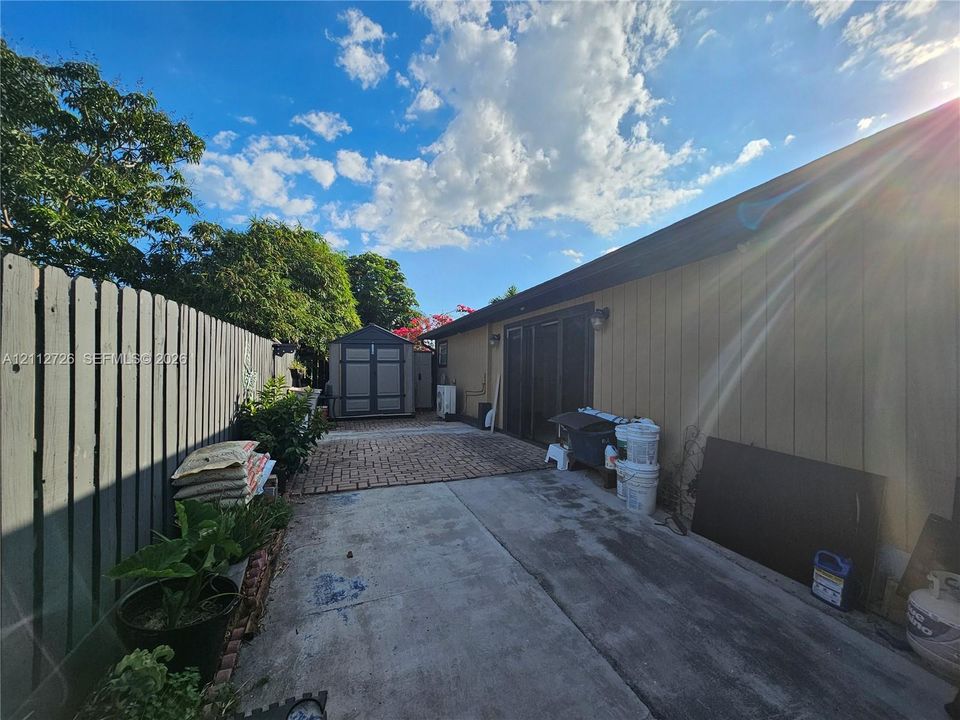 Exterior space featuring a brick-paved patio, a concrete side path, a vertical-panel wood fence, and a detached storage structure