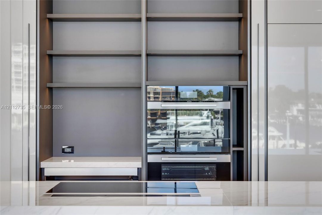 Floor-to-ceiling cabinetry with open shelving, integrated stainless steel double wall ovens, smooth-surface cooktop, and stone countertop