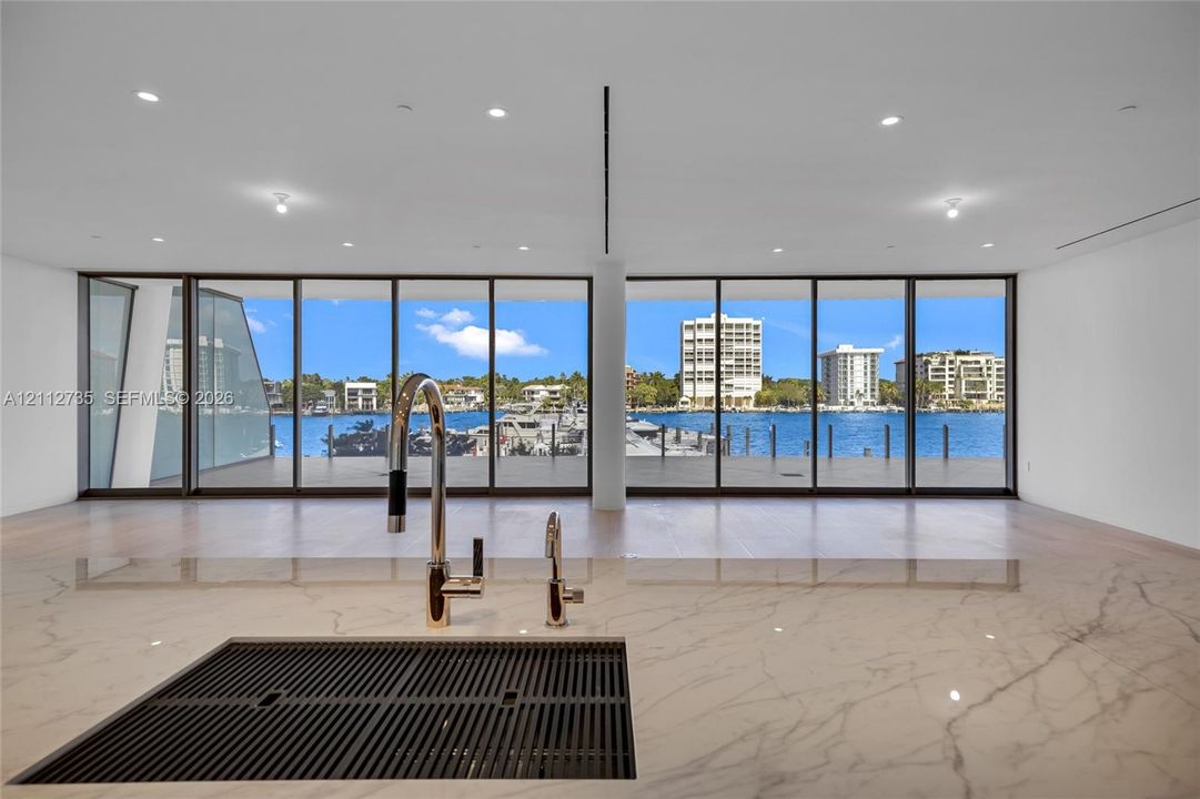 Countertop with an integrated drainboard and high-arc faucet, wood-finish flooring, and expansive floor-to-ceiling glass panels overlooking the waterfront