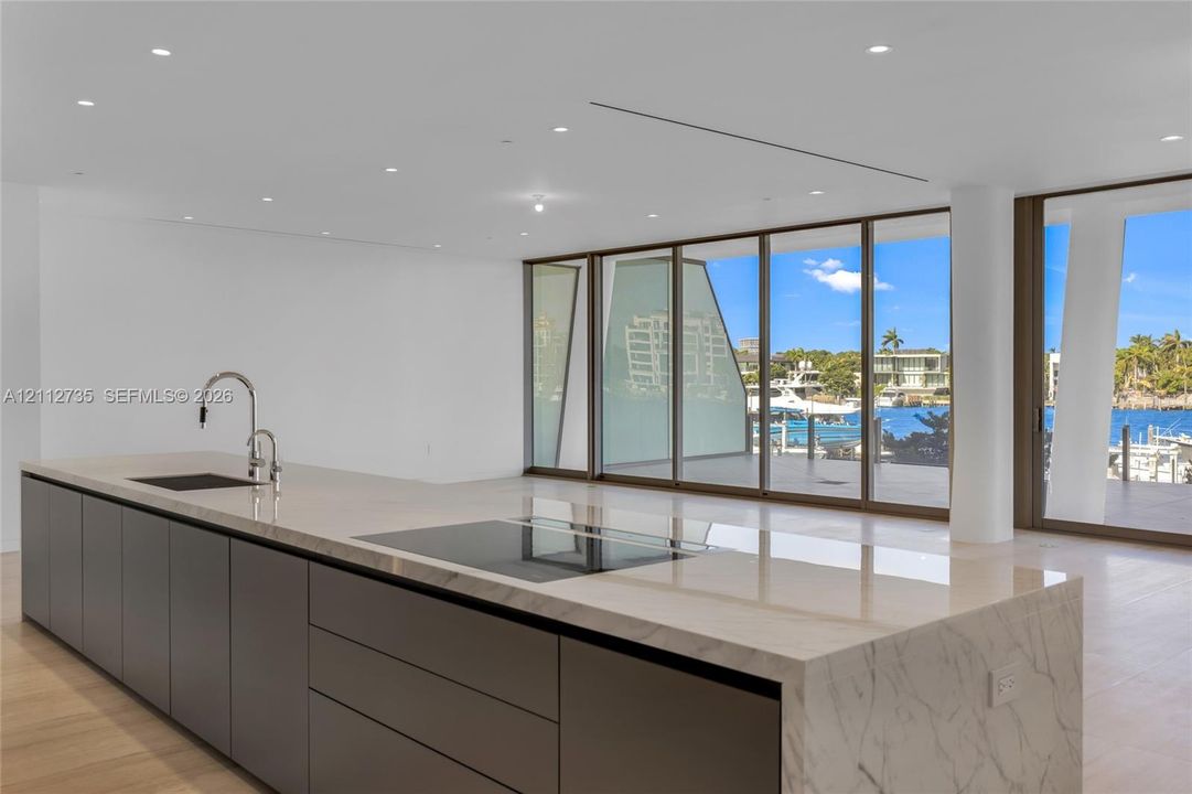 Kitchen island featuring a waterfall stone countertop, integrated cooktop, recessed lighting, floor-to-ceiling glass wall, and wood-finish flooring
