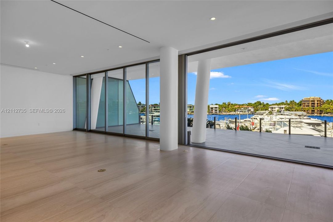 Floor-to-ceiling retractable glass walls, wide-plank wood-finish flooring, recessed lighting, and expansive covered balcony with tile surfacing
