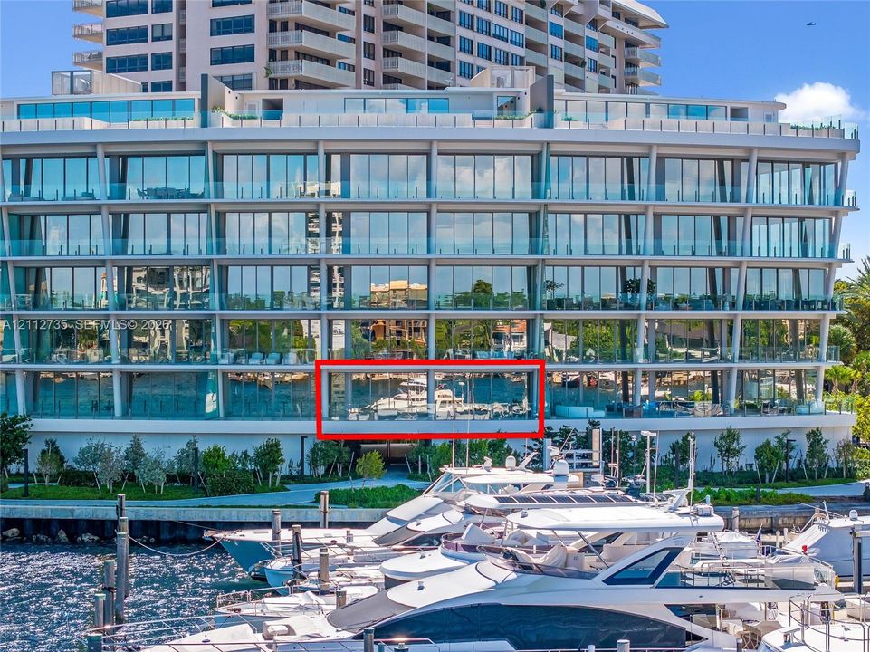 Multi-story contemporary exterior featuring floor-to-ceiling glass paneling, horizontal cantilevered balconies with glass railings, and a deep-water marina