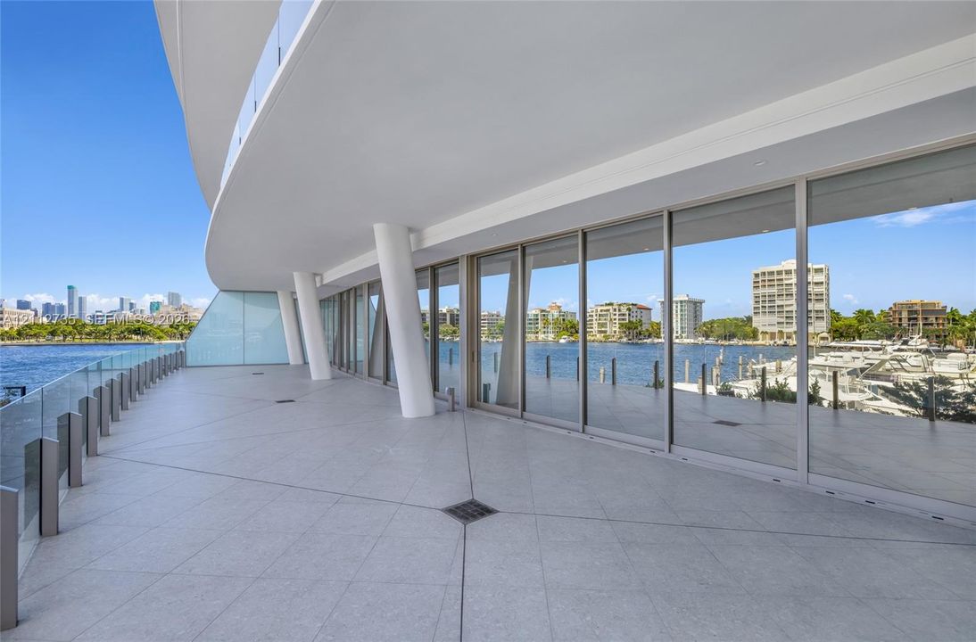 Expansive wraparound balcony featuring large-format tile flooring, a glass railing system, structural architectural pillars, and floor-to-ceiling glass wall panels