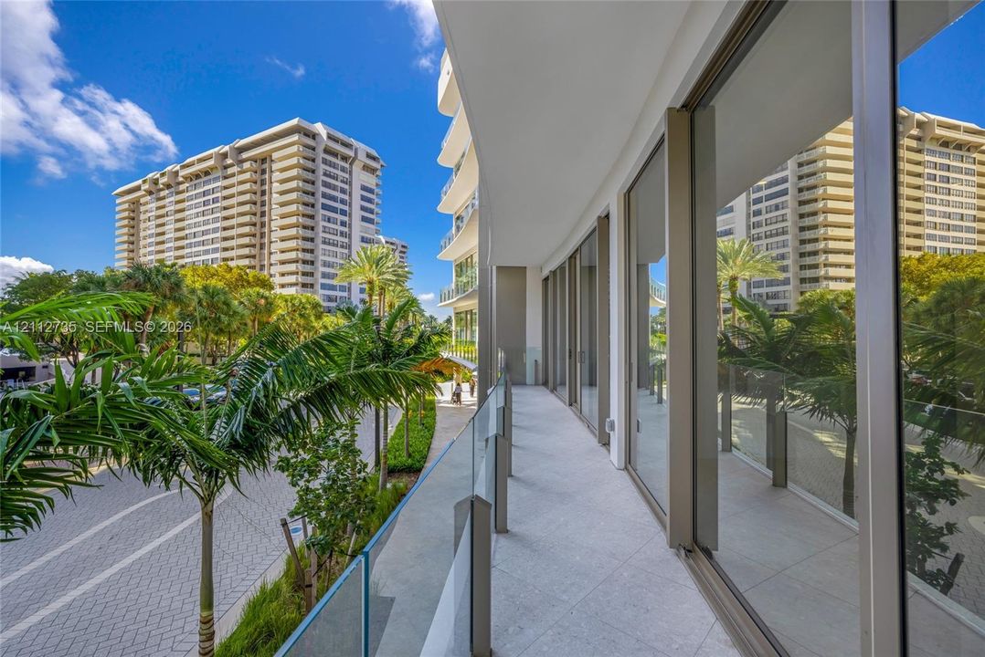 Curved balcony featuring light-toned stone flooring, floor-to-ceiling glass panel railings, and expansive glass wall paneling