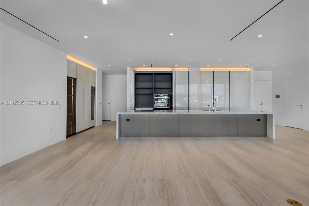 Modern kitchen featuring floor-to-ceiling cabinetry, a sprawling central island with stone-finish countertops, built-in dual wall ovens, recessed linear lighting, and large-format tile flooring