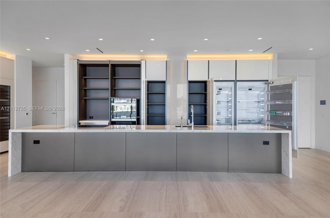 Large kitchen island featuring a stone waterfall countertop, integrated refrigeration, floor-to-ceiling cabinetry with open shelving, recessed lighting, and wood-finish flooring