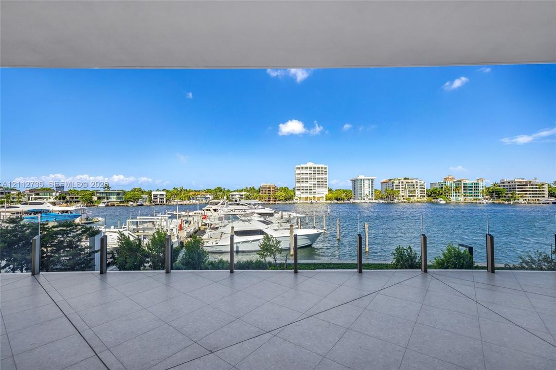 Covered terrace featuring large-format porcelain tile flooring and a transparent glass railing overlooking the waterfront