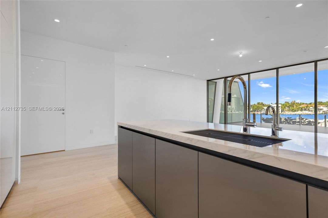 Kitchen island featuring flat-panel cabinetry, light-toned stone-finish countertop, integrated sink, and polished metal faucet, complemented by wood-finish flooring and floor-to-ceiling windows