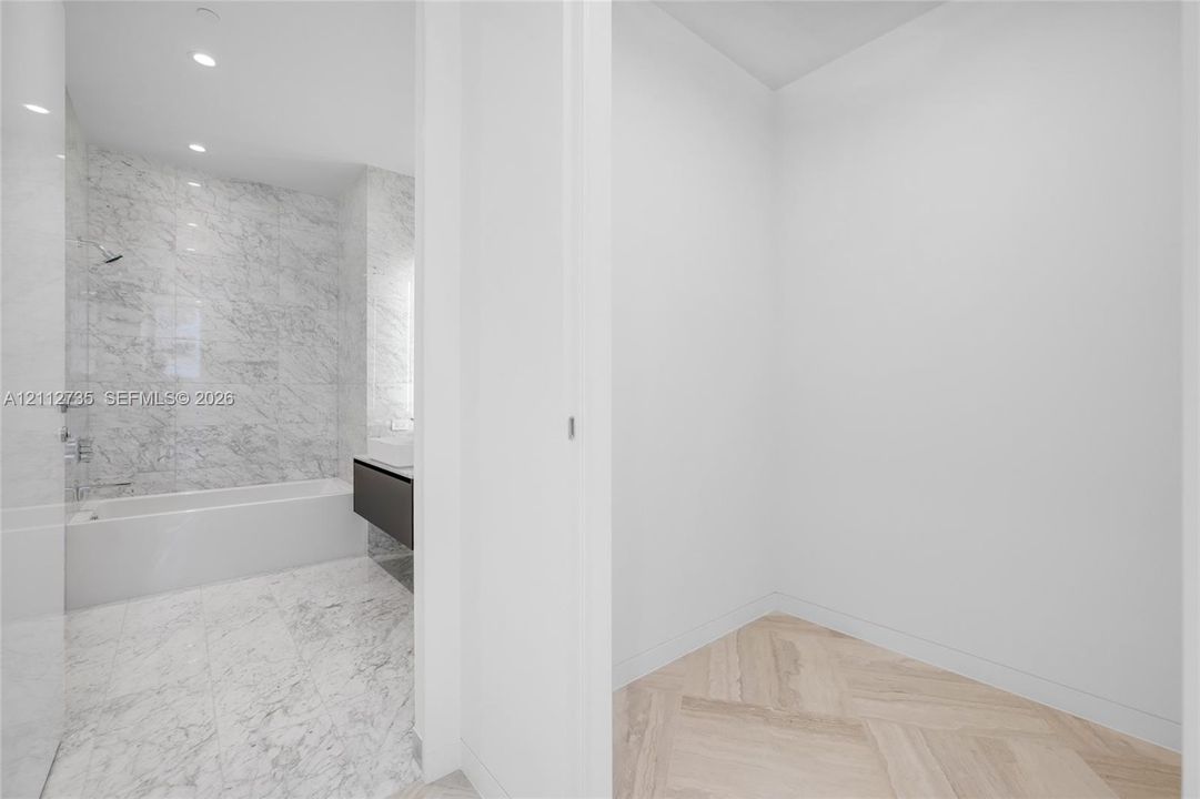 Bathroom featuring stone-finish wall and floor tiling, a soaking tub with integrated shower hardware, a floating vanity with a vessel sink, and herringbone-pattern wood-finish flooring