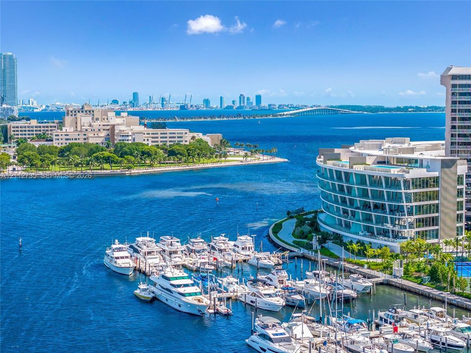 Aerial perspective of a deep-water marina featuring boat slips and a curved modern mid-rise building with floor-to-ceiling glass paneling and balcony tiers