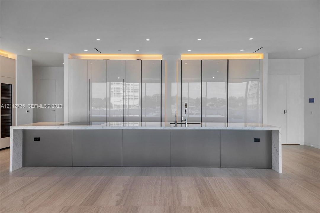 Kitchen featuring floor-to-ceiling high-gloss cabinetry, a large central island with a stone-finish waterfall countertop, integrated faucet fixtures, recessed ceiling lighting, and wood-finish flooring
