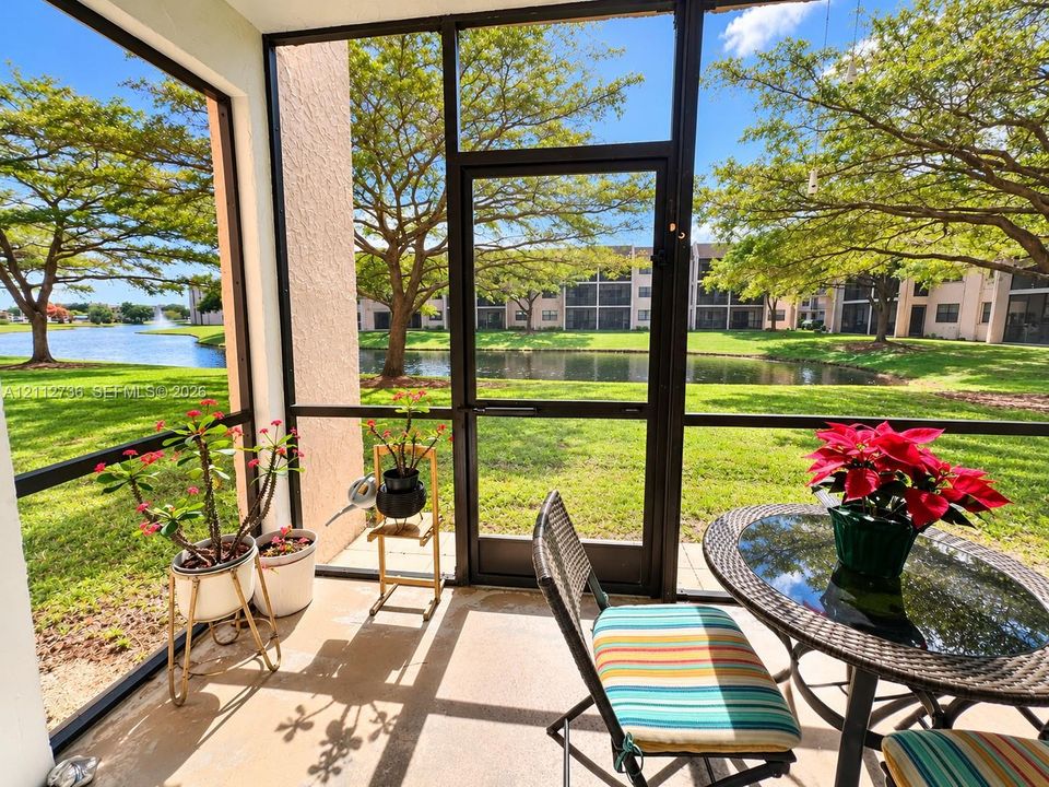 Screened-in patio with concrete flooring, framed by metal enclosure and situated overlooking a pond and manicured lawn