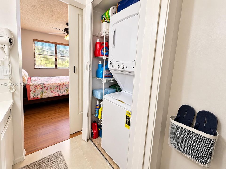 Laundry closet featuring a stackable washer and dryer unit with integrated wire shelving and a sliding door