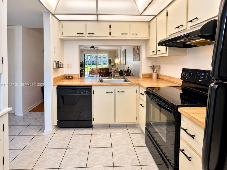 Kitchen featuring wood-finish countertops, black appliances, tile flooring, recessed tray ceiling lighting, and ample cabinetry with matte black hardware