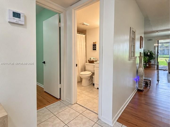 Ceramic tile flooring, digital wall-mounted thermostat, and bathroom with a pedestal sink and shower-tub combination