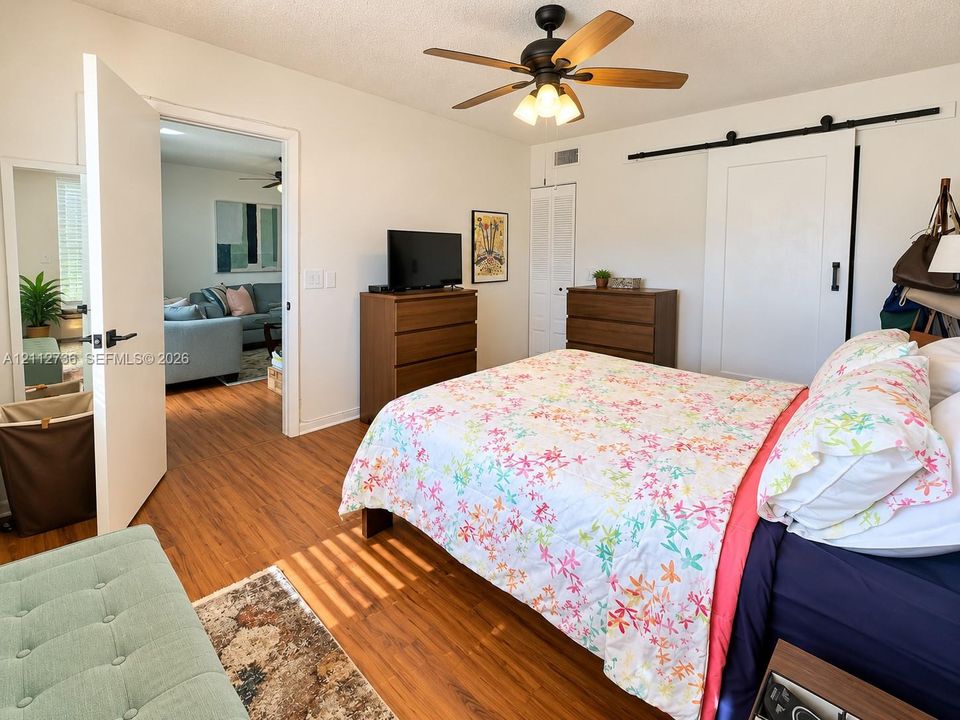 Room featuring wood-finish flooring, a ceiling fan with integrated lighting, and a white sliding barn door on a black metal track