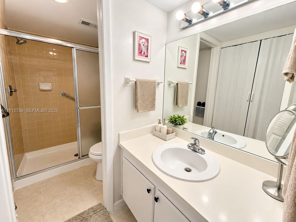 Bathroom featuring a single-sink vanity with a solid-surface countertop, full-width vanity mirror, over-mirror lighting, and a glass-enclosed shower with tile surround