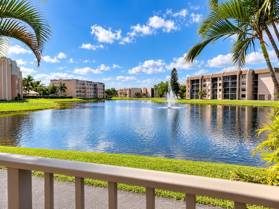 Waterfront setting featuring a central fountain, manicured lawn, and mature palm trees