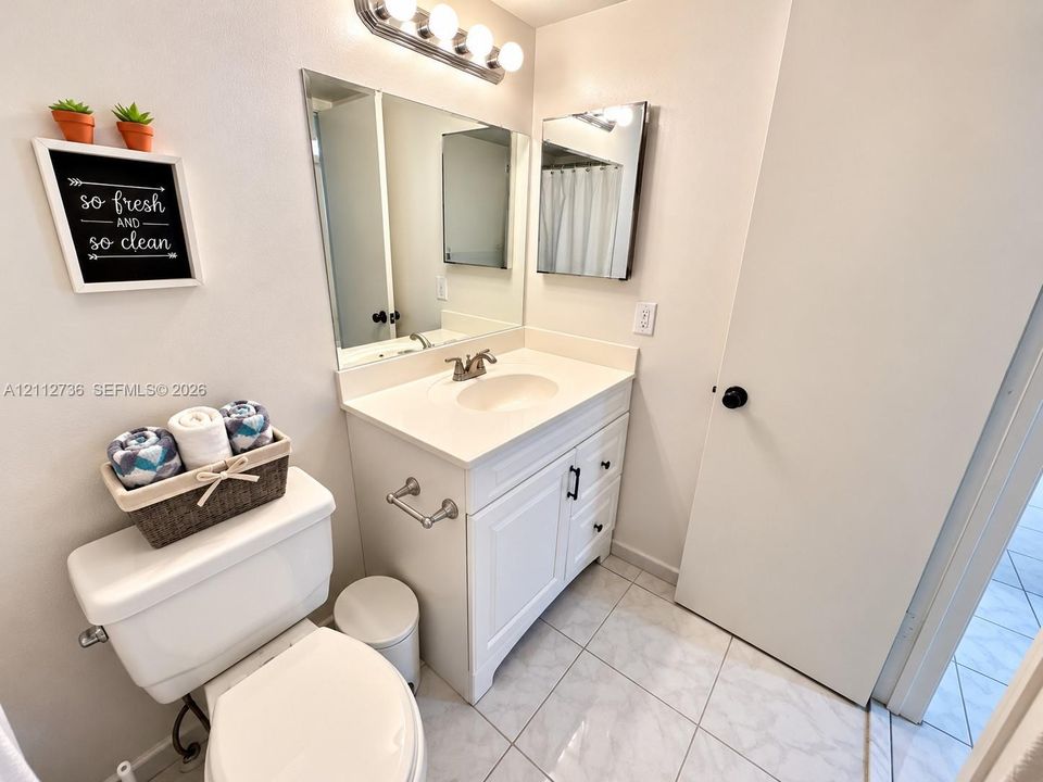 Bathroom featuring a white vanity cabinet, solid-surface countertop with an integrated basin, wall-mounted vanity lighting, a large rectangular mirror, and tile flooring