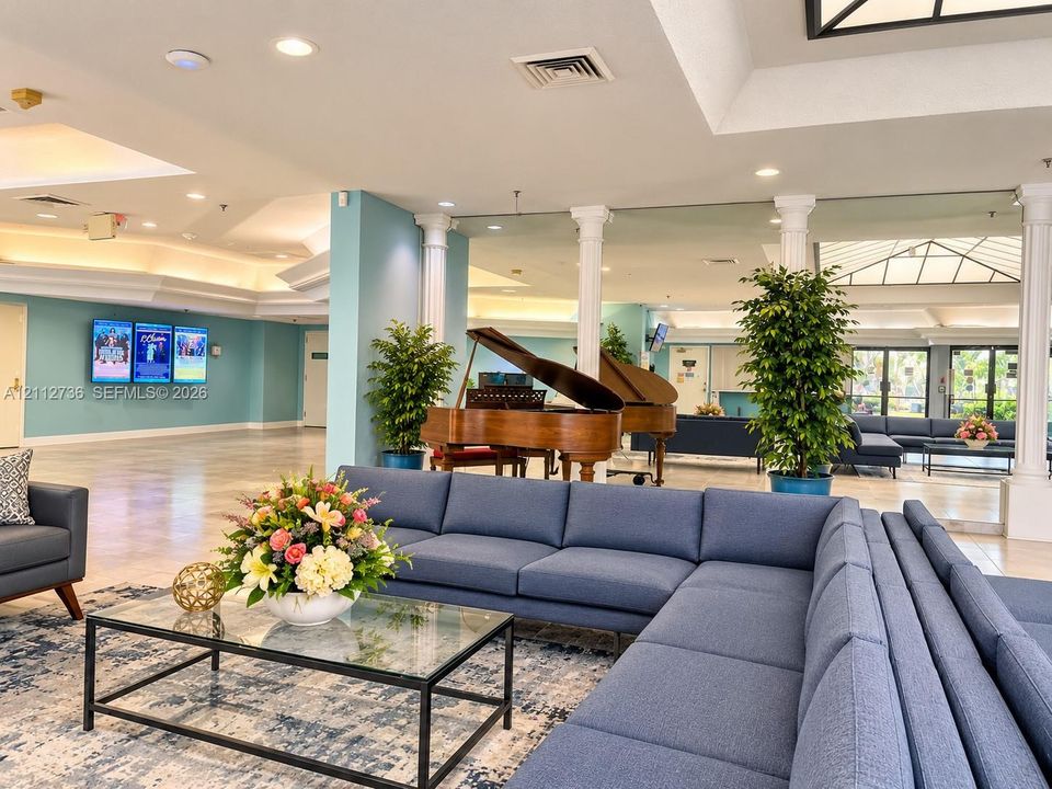 Open-concept common area featuring structural columns, tray ceilings with recessed lighting, mirrored wall accents, and an expansive skylight