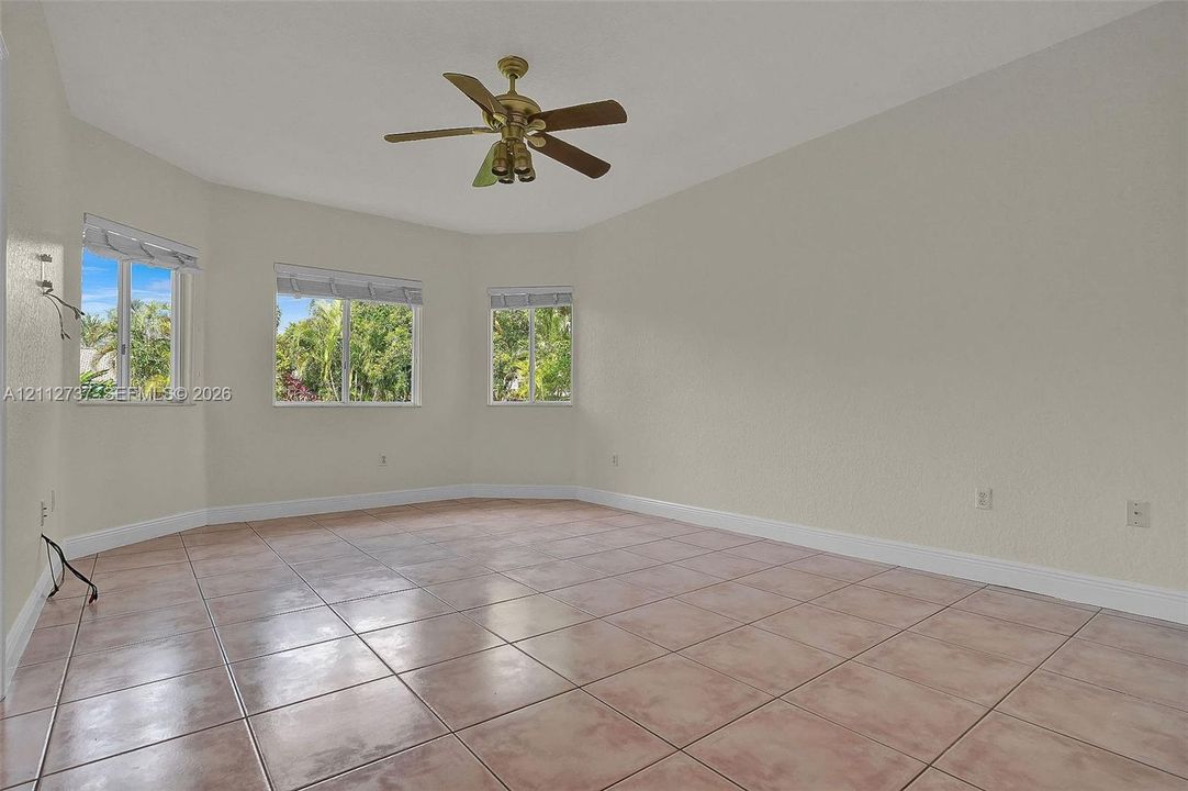 Spacious room featuring neutral wall tones, ceramic tile flooring, three large windows, and a multi-blade ceiling fan with integrated lighting
