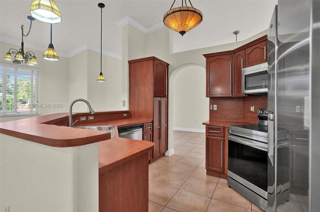 Kitchen featuring wooden cabinetry, stainless steel appliances, ceramic tile flooring, a wrap-around counter, and multi-light pendant fixtures