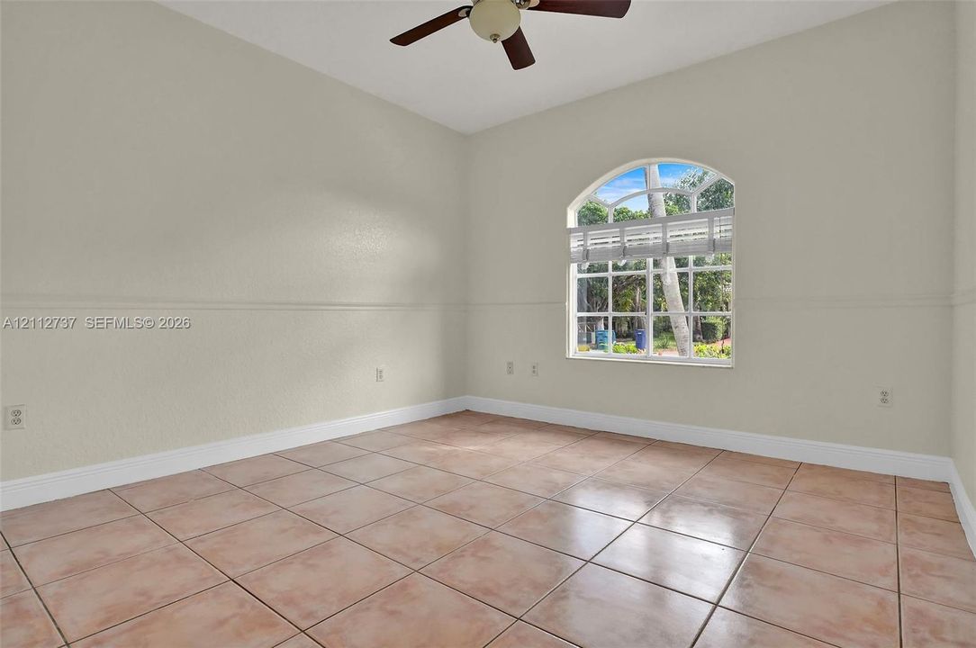 Interior room featuring large-format ceramic tile flooring, an arched window with muntin detailing, neutral wall finishes with chair rail molding, and a ceiling-mounted fan