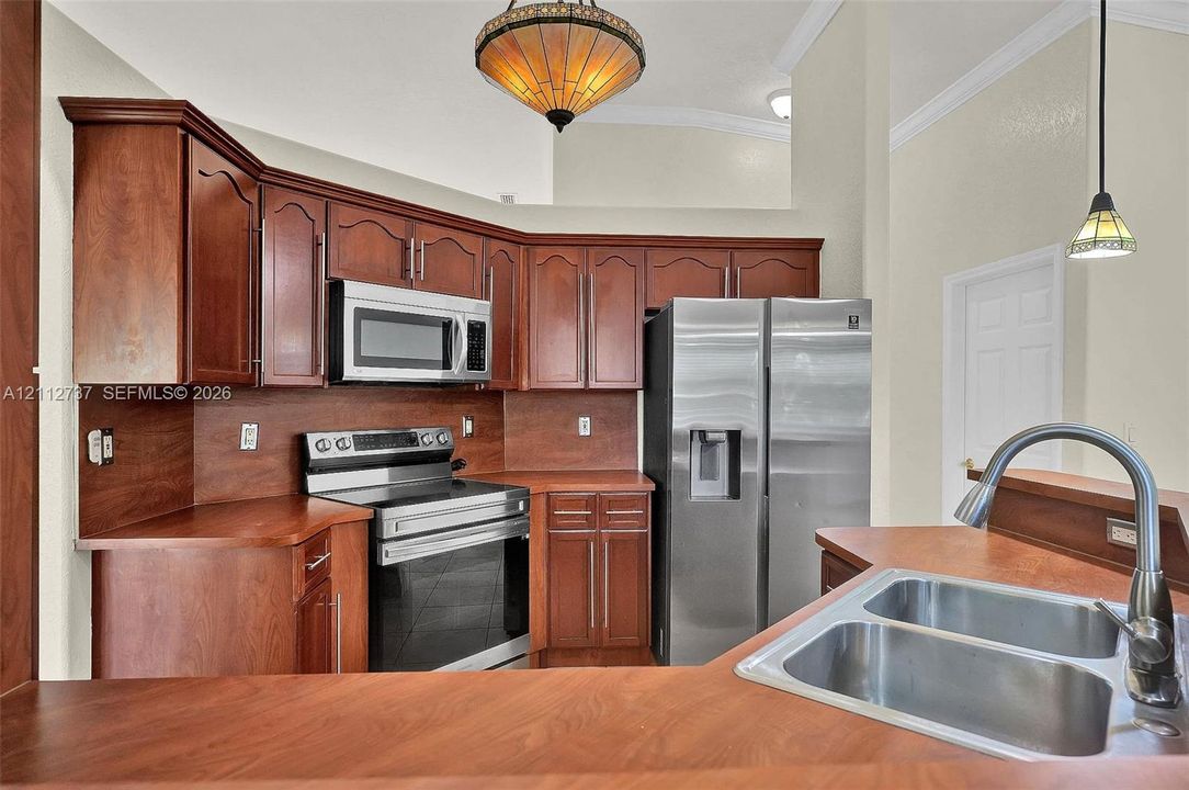 Kitchen featuring cherry-toned cabinetry, stainless steel appliances, a double-basin under-mount sink, high-vaulted ceilings, and multi-light pendant fixtures