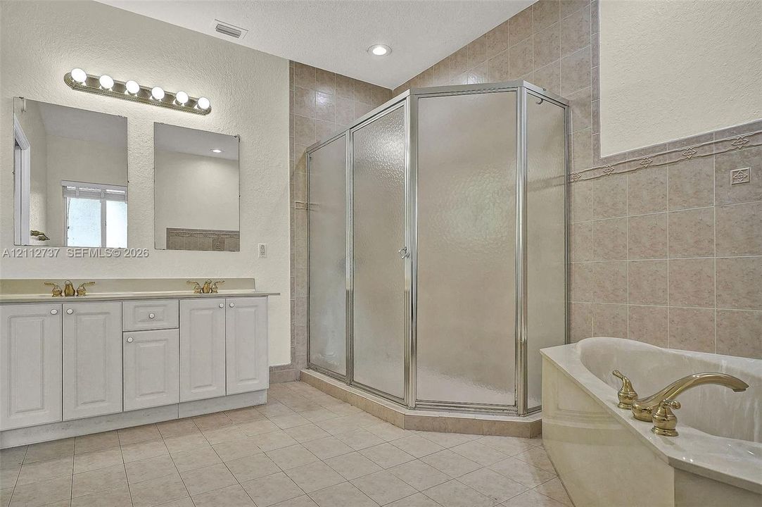 Dual vanity with white cabinetry, corner shower enclosure with glass panels, separate soaking tub, and tile flooring