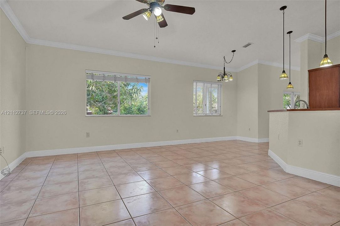 Open living area featuring large-format ceramic tile flooring, crown molding, a central ceiling fan with integrated lighting, and multiple pendant lights over a breakfast bar