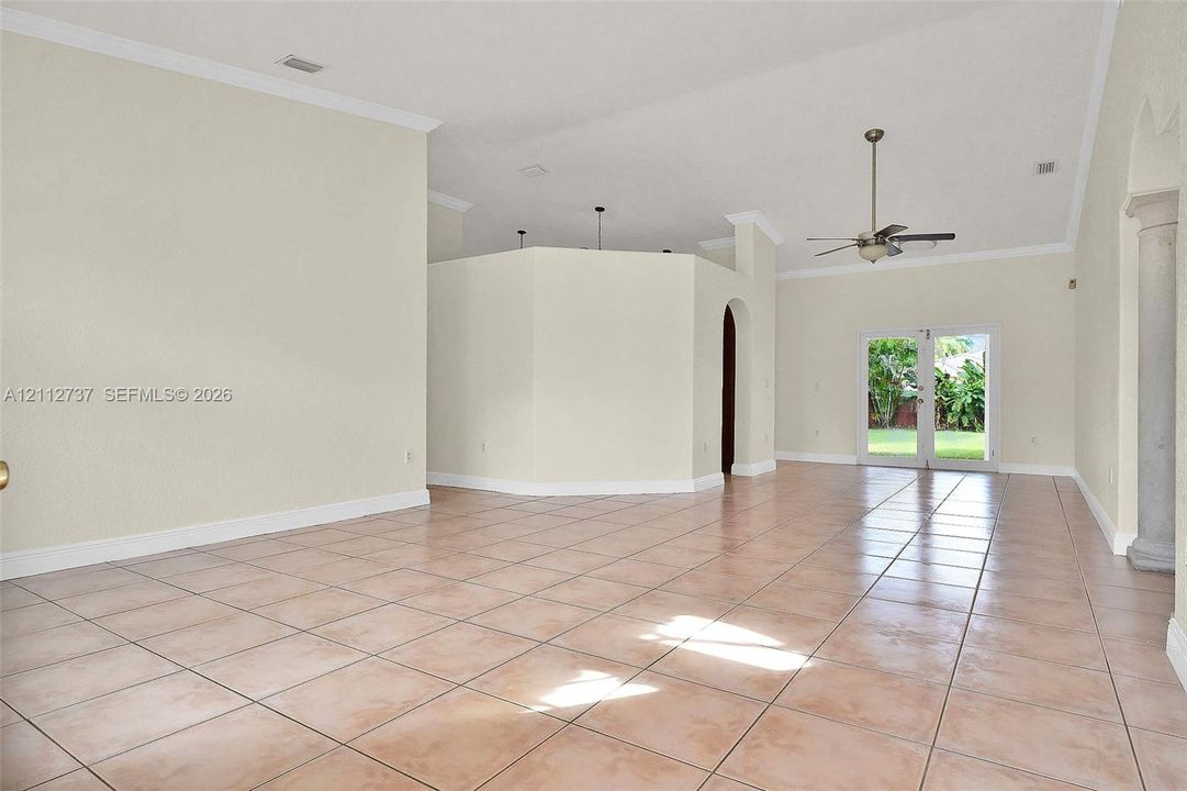 Open-concept interior featuring vaulted ceilings, ceramic tile flooring, a decorative column, and dual glass-paned doors