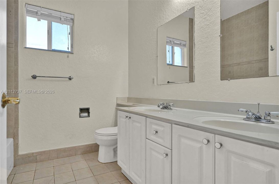 Dual-sink vanity with white cabinetry, light-toned countertop, and rectangular wall-mounted mirrors, complemented by tile flooring