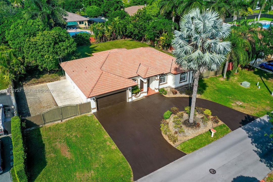 Single-story residence featuring a tiled roof, multi-car garage, expansive paved driveway, and established landscaping