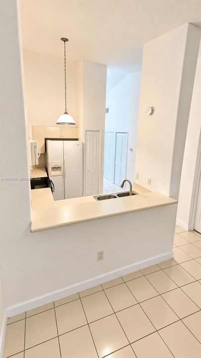 Kitchen featuring a pass-through counter, double-basin stainless steel sink, tile flooring, built-in cabinetry, and a pendant light fixture