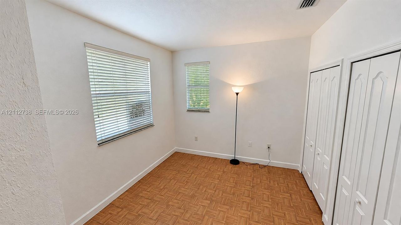 Room featuring parquet wood-finish flooring, two windows with horizontal blinds, and dual bi-fold closet doors