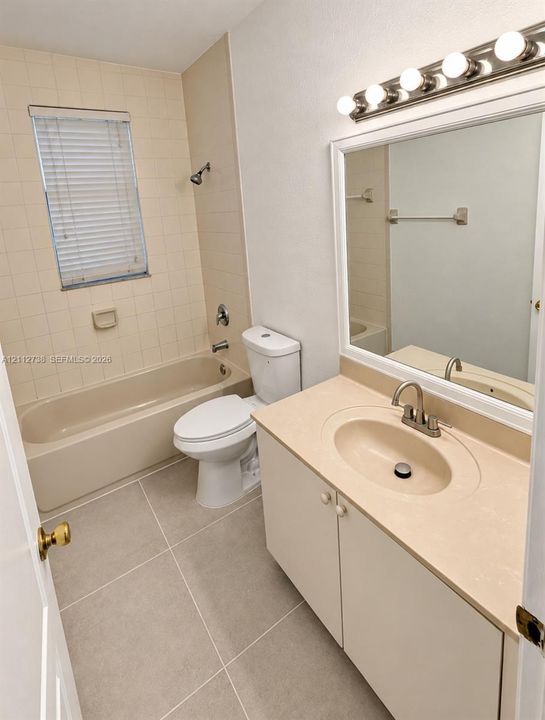 Bathroom featuring large-format tile flooring, a vanity with a solid-surface countertop and integrated sink, a wall-mounted mirror with a white frame, and a five-light vanity fixture